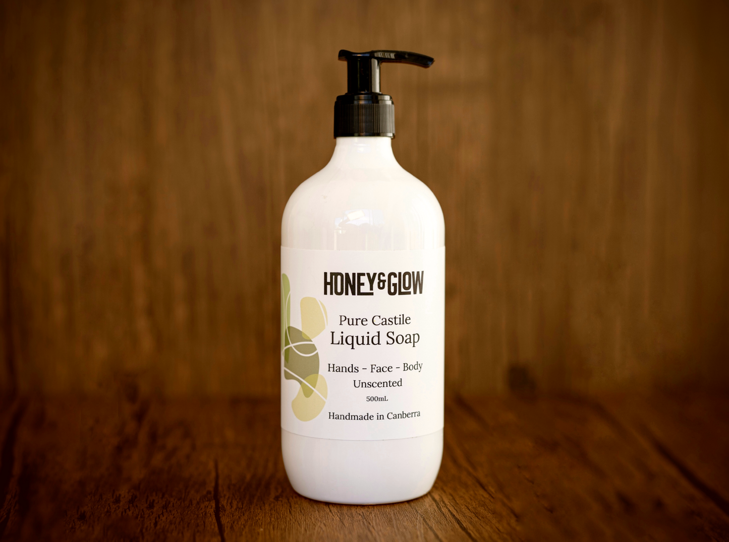 White bottle of pure castile liquid soap by Honey and Glow, styled on a timber background
